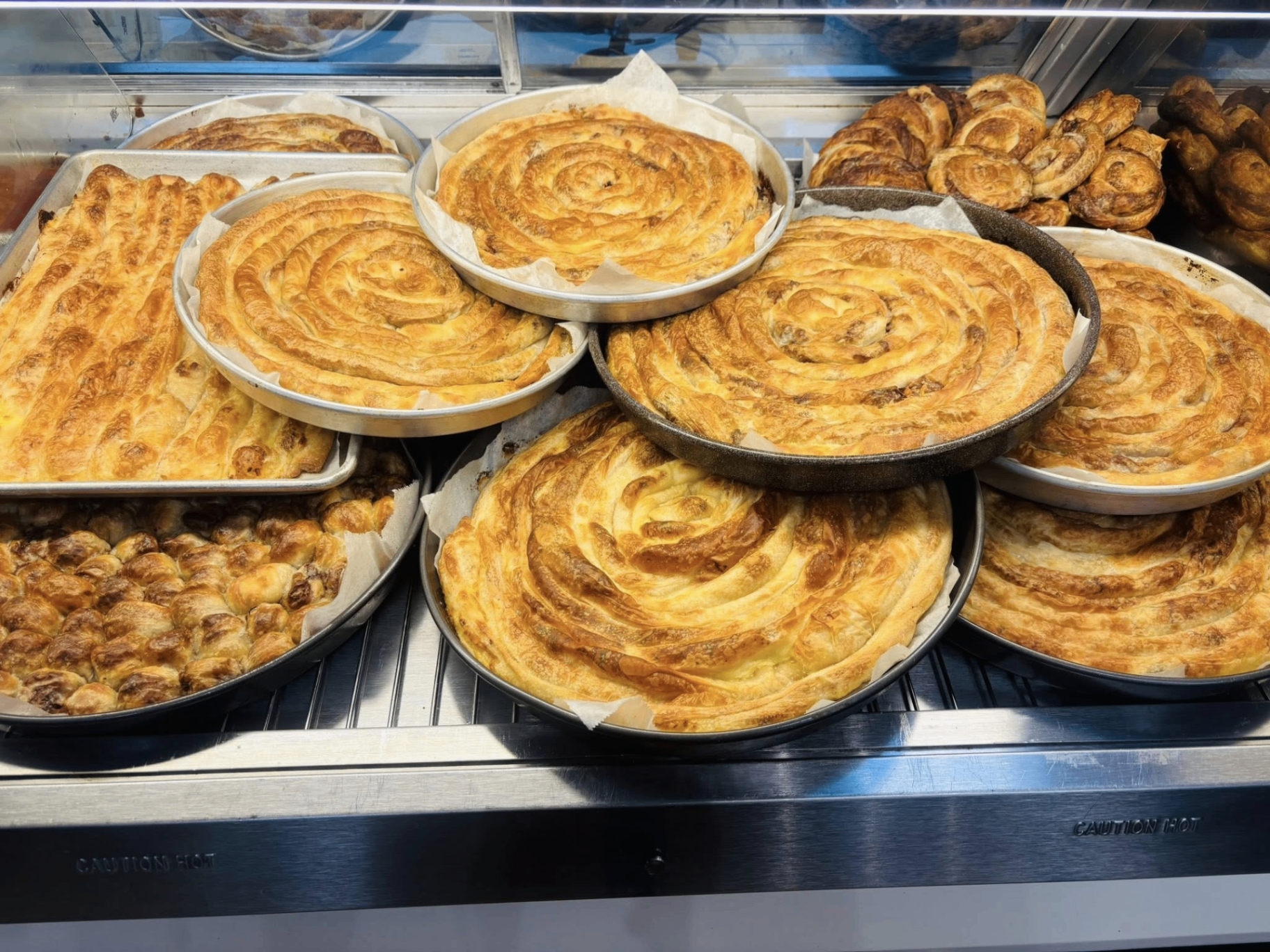 Bakery case full of round burek, sirnica and krompiruša pans