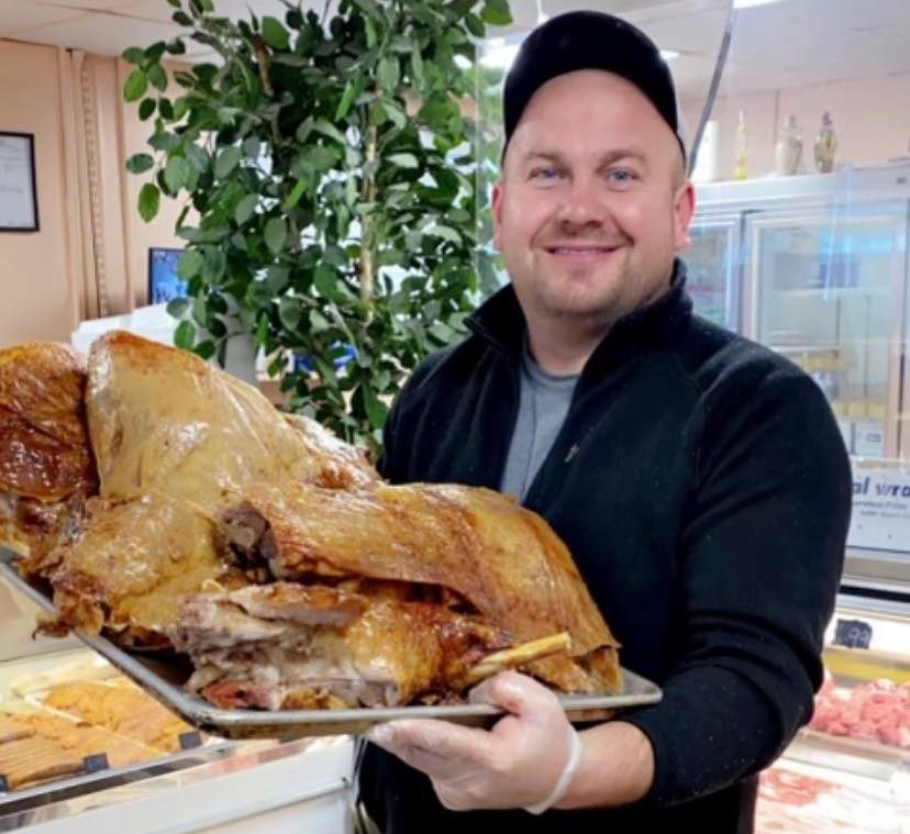 Alen behind the counter holding a tray of freshly roasted halal lamb
