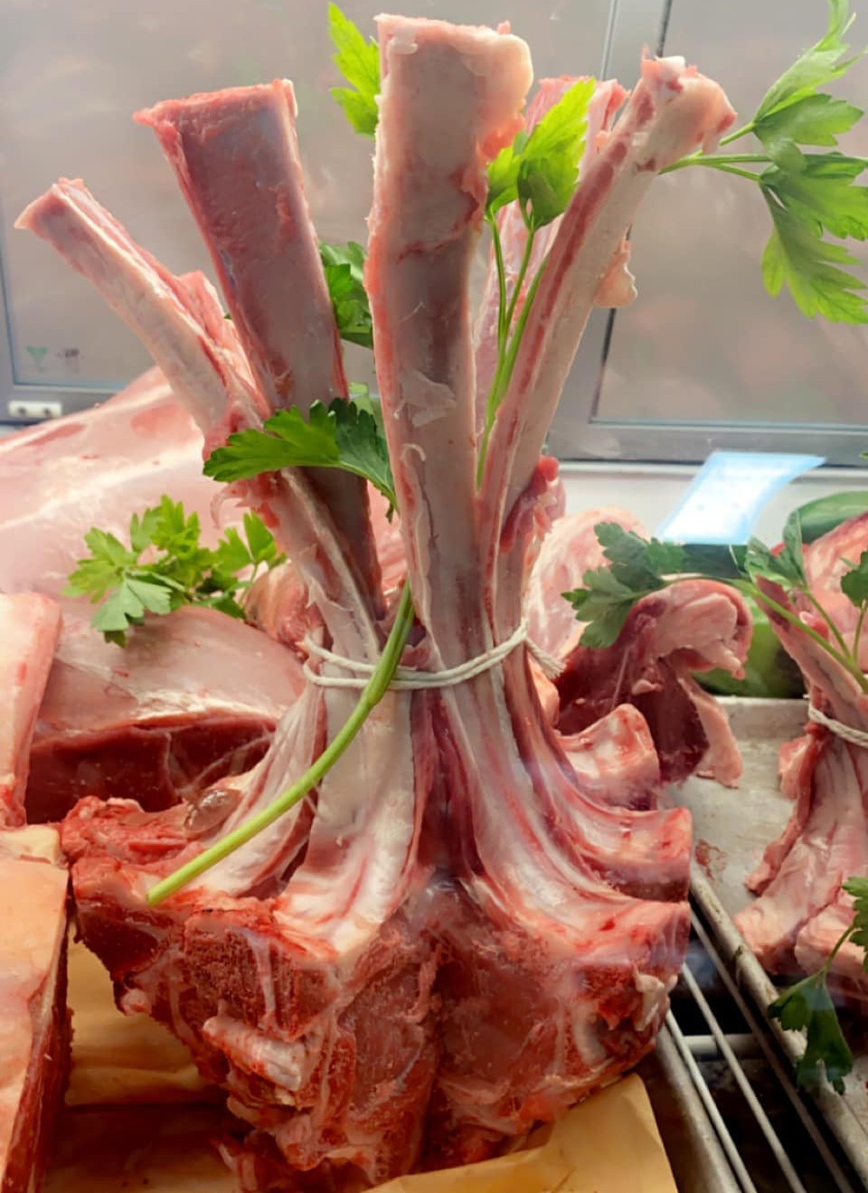 Bundle of frenched lamb rib chops tied upright with twine and garnished with parsley in the meat case