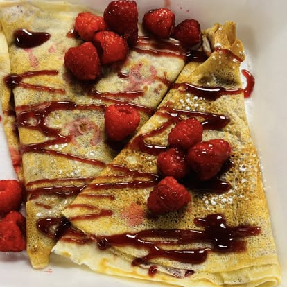Folded crepes drizzled with raspberry sauce and fresh berries