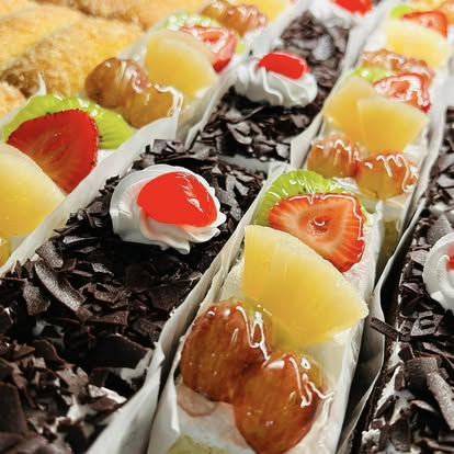 Rows of fresh fruit tart slices with strawberries, kiwi and pineapple
