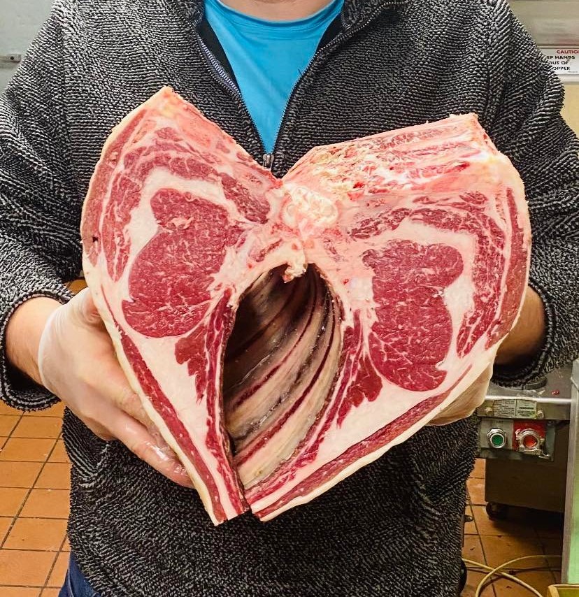 Butcher holding a freshly cut beef rib rack showing the marbled ribeye cross-section
