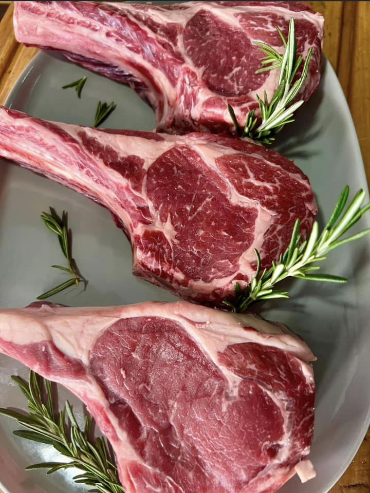 Three thick bone-in ribeye steaks with rosemary sprigs on a platter