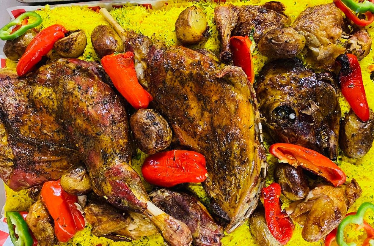 Roasted lamb and chicken platter served over saffron rice with roasted peppers and potatoes